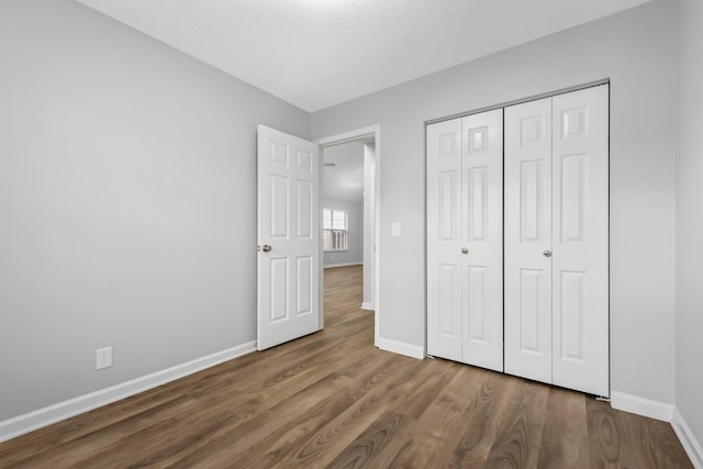 unfurnished bedroom with baseboards, wood finished floors, and a closet