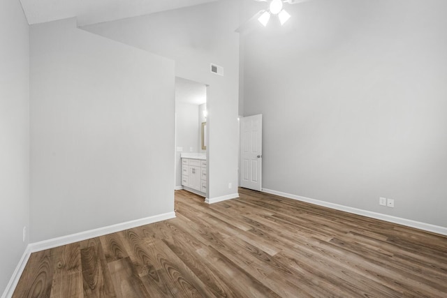 unfurnished bedroom with wood finished floors, baseboards, connected bathroom, high vaulted ceiling, and a ceiling fan