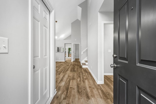 entryway featuring wood finished floors, baseboards, stairway, and vaulted ceiling