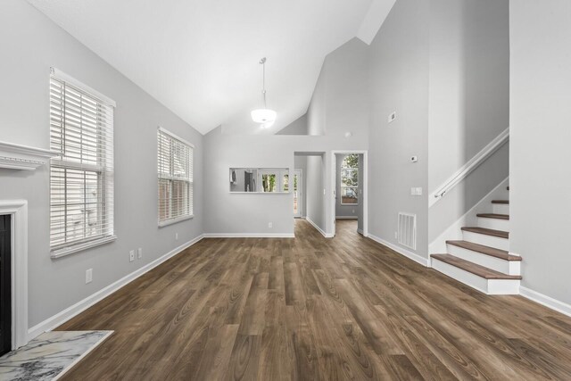 unfurnished living room featuring wood finished floors, healthy amount of natural light, stairway, baseboards, and high vaulted ceiling