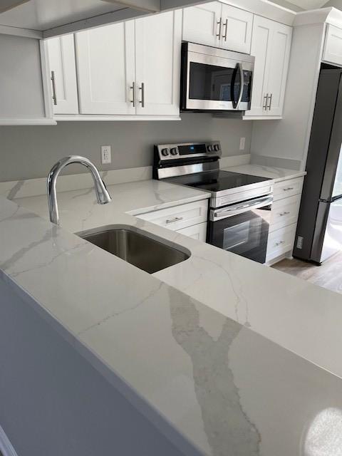 kitchen featuring appliances with stainless steel finishes, a sink, white cabinetry, light stone countertops, and light wood-style flooring