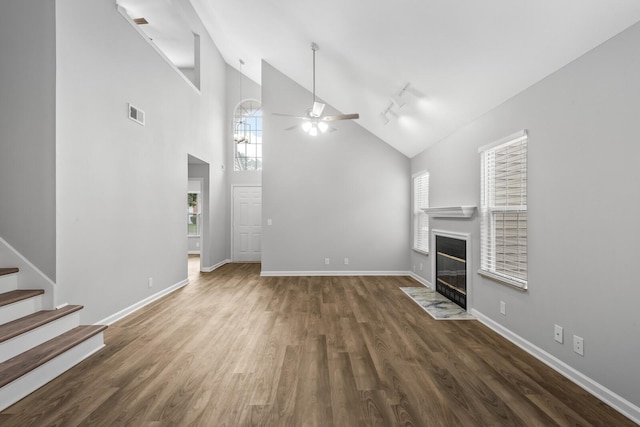 unfurnished living room featuring a ceiling fan, wood finished floors, baseboards, a fireplace with flush hearth, and high vaulted ceiling