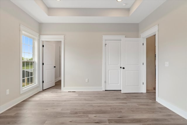 unfurnished bedroom with light wood-style floors, visible vents, baseboards, and a raised ceiling