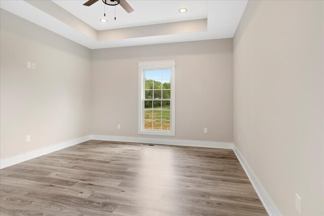 empty room with baseboards, a ceiling fan, wood finished floors, and a raised ceiling