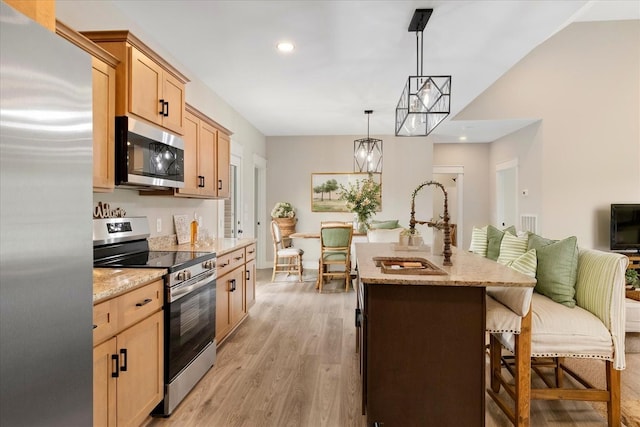 kitchen with light stone countertops, stainless steel appliances, light brown cabinets, and a kitchen breakfast bar
