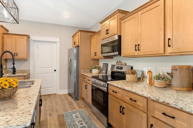 kitchen with a sink, recessed lighting, light wood-style floors, light stone counters, and appliances with stainless steel finishes