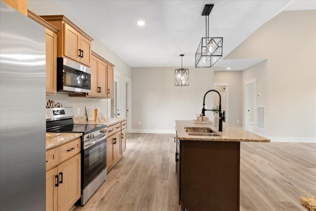 kitchen with light wood-style flooring, a sink, a center island with sink, light brown cabinets, and appliances with stainless steel finishes