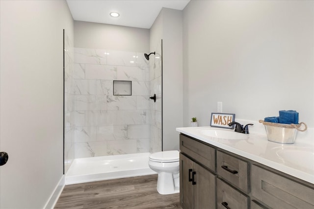 bathroom with a sink, double vanity, a tile shower, toilet, and wood finished floors