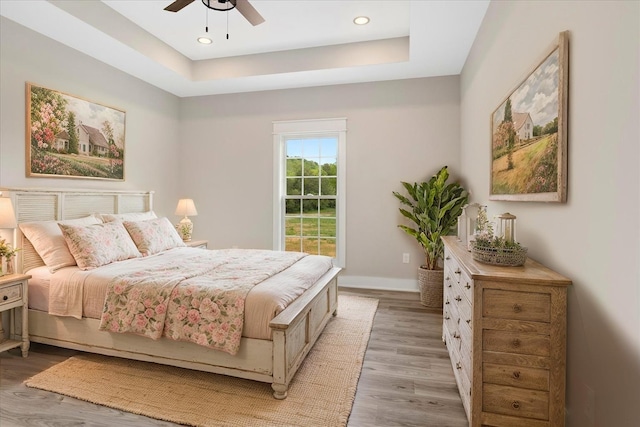 bedroom with recessed lighting, a tray ceiling, a ceiling fan, light wood-style floors, and baseboards