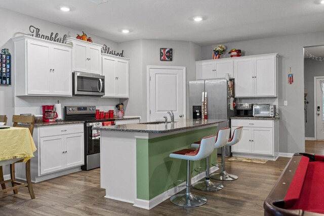 kitchen featuring wood finished floors, appliances with stainless steel finishes, white cabinetry, and a sink