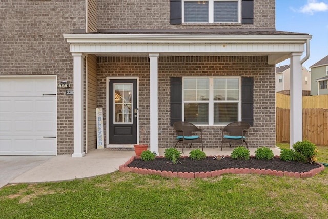property entrance featuring fence, a yard, covered porch, brick siding, and a garage