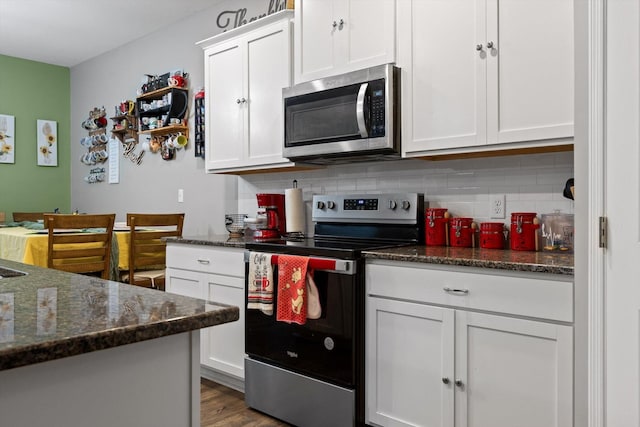 kitchen featuring white cabinets, stainless steel appliances, dark stone countertops, and backsplash