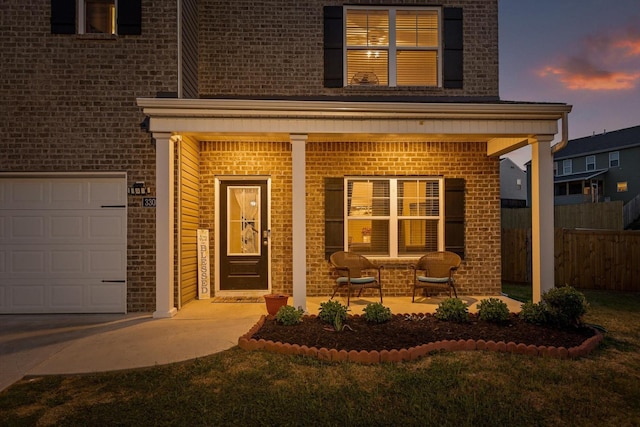 exterior entry at dusk with brick siding, a porch, and fence