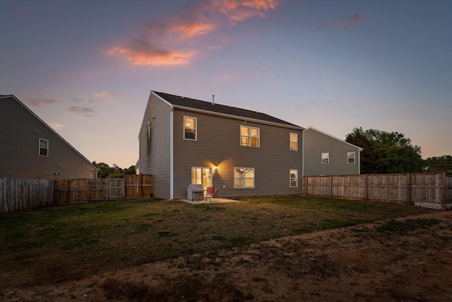 back of house at dusk with a fenced backyard, a gate, a patio area, and a yard