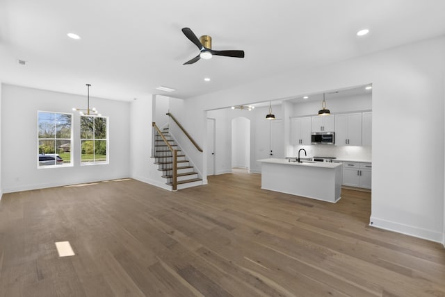 unfurnished living room featuring baseboards, arched walkways, recessed lighting, and stairway