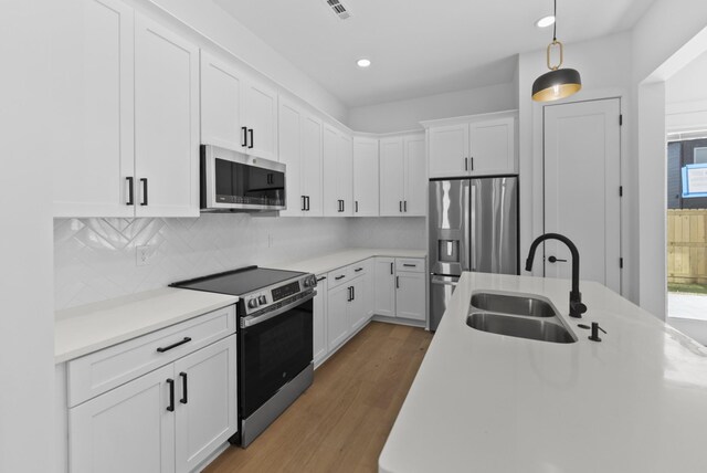 kitchen with white cabinets, stainless steel appliances, a sink, light wood-type flooring, and pendant lighting