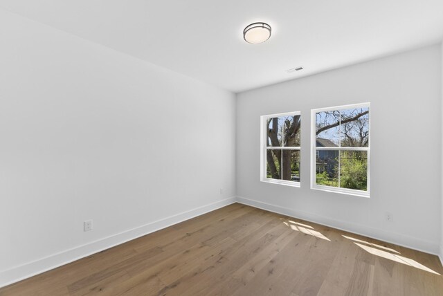 empty room with baseboards, wood finished floors, and visible vents