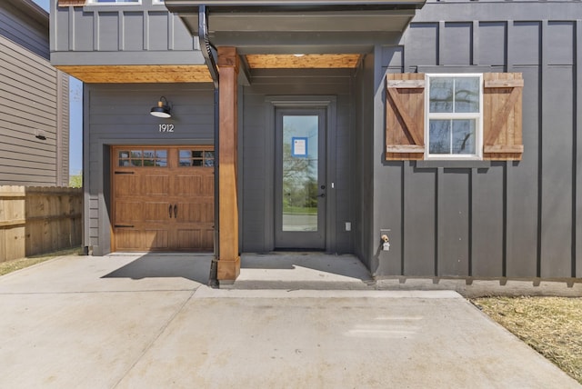 view of exterior entry with fence, a garage, board and batten siding, and driveway