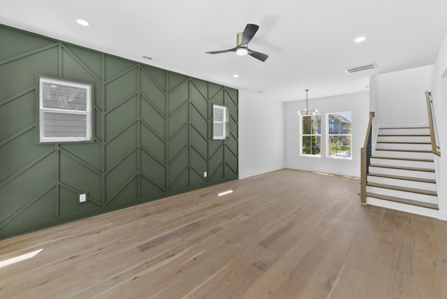 empty room with light wood-type flooring, baseboards, visible vents, stairs, and a decorative wall