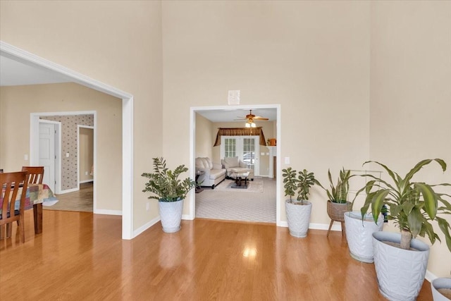 hallway with baseboards, wood finished floors, and a high ceiling