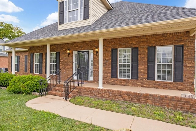 property entrance with a porch, a shingled roof, and brick siding