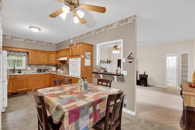 dining room featuring light colored carpet, a ceiling fan, and baseboards