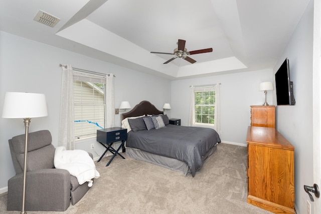 bedroom with a tray ceiling, light colored carpet, baseboards, and a ceiling fan