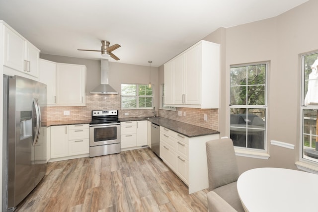 kitchen featuring appliances with stainless steel finishes, wall chimney range hood, dark countertops, light wood-style floors, and decorative backsplash