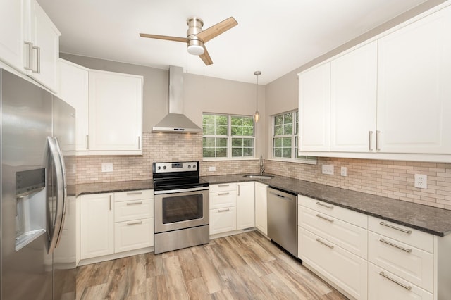 kitchen featuring appliances with stainless steel finishes, wall chimney range hood, a sink, a ceiling fan, and tasteful backsplash