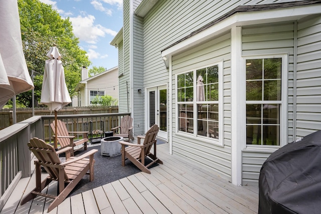 wooden terrace with a fire pit, fence, and area for grilling