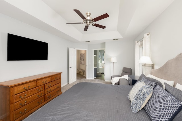 bedroom with a tray ceiling, light carpet, ensuite bath, baseboards, and a ceiling fan