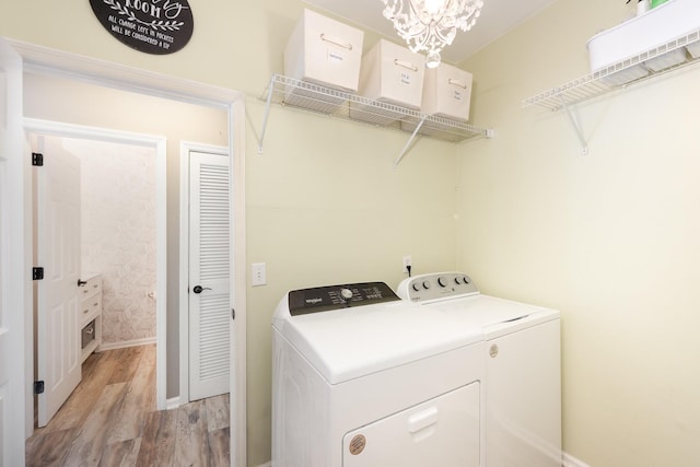 clothes washing area featuring washer and clothes dryer, light wood finished floors, baseboards, and a chandelier