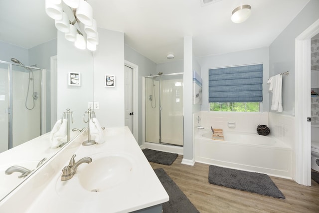 bathroom featuring a stall shower, wood finished floors, a bath, double vanity, and toilet