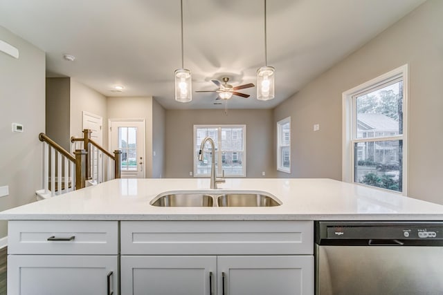 kitchen featuring light stone countertops, stainless steel dishwasher, a sink, and hanging light fixtures