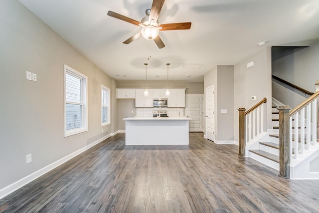 unfurnished living room featuring baseboards, dark wood-style floors, stairs, and ceiling fan