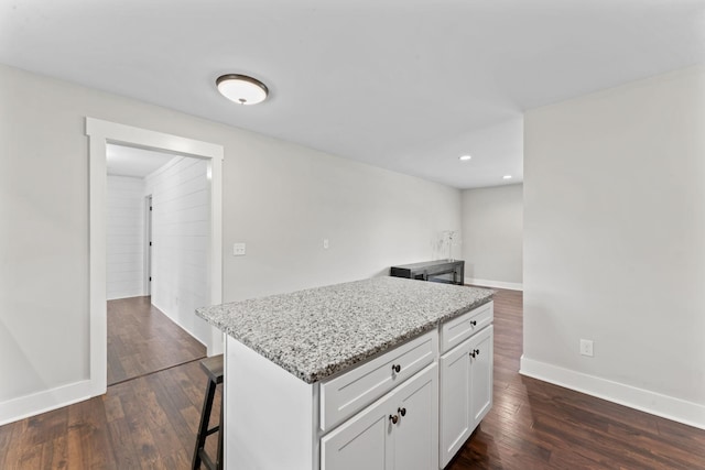 kitchen featuring white cabinets, light stone countertops, a kitchen breakfast bar, dark wood finished floors, and recessed lighting