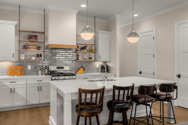 kitchen featuring a sink, a center island with sink, open shelves, stainless steel gas range oven, and premium range hood