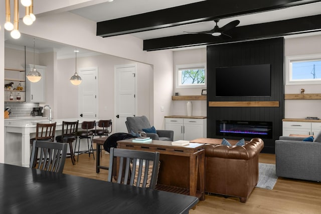living room featuring a large fireplace, a ceiling fan, beam ceiling, and light wood-style floors