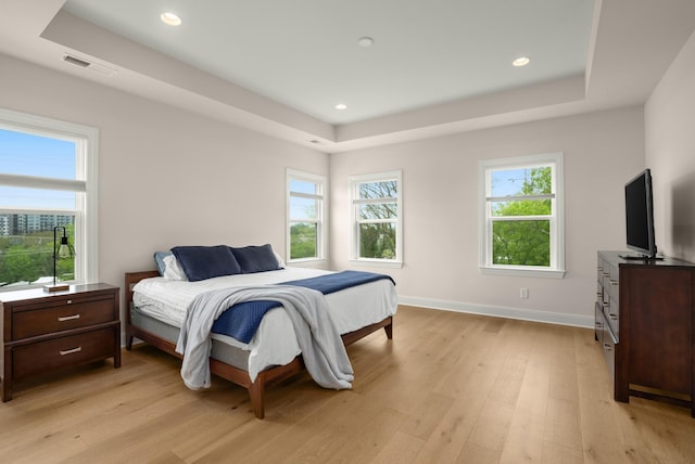 bedroom featuring light wood-style flooring, multiple windows, visible vents, and a raised ceiling