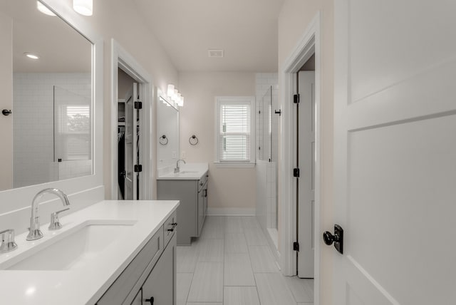 bathroom with a tile shower, two vanities, a sink, and baseboards