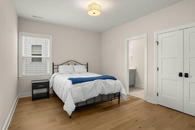 bedroom featuring visible vents, baseboards, light wood-style floors, a closet, and ensuite bath