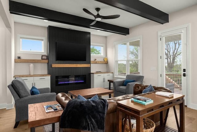 living area with a ceiling fan, beamed ceiling, light wood-style floors, baseboards, and a fireplace