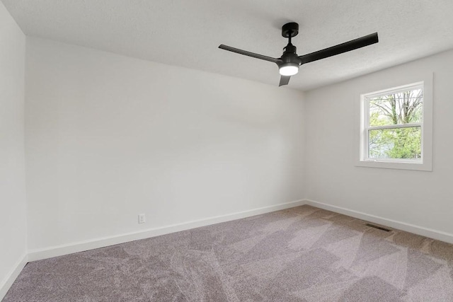 carpeted spare room with visible vents, baseboards, and ceiling fan
