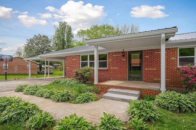doorway to property featuring brick siding, driveway, covered porch, and metal roof