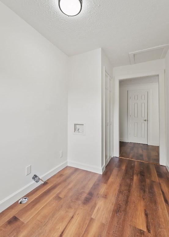 unfurnished room featuring attic access, baseboards, wood finished floors, and a textured ceiling