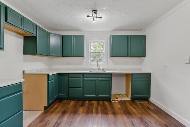 kitchen with green cabinetry, dark wood-style floors, ornamental molding, a sink, and a textured ceiling
