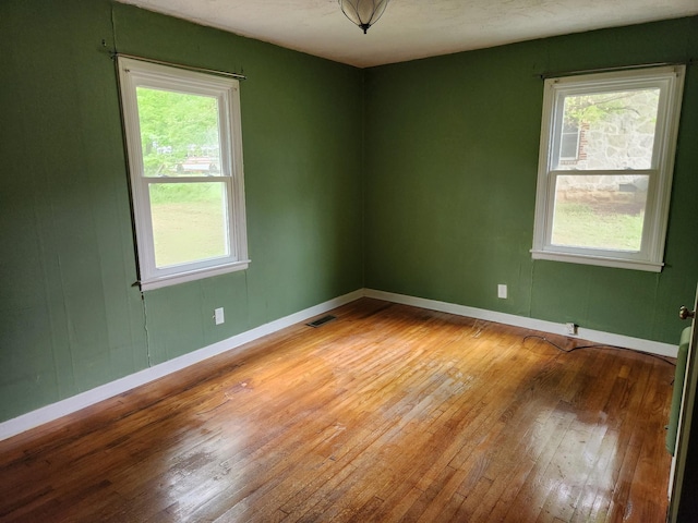 empty room with hardwood / wood-style flooring, baseboards, and visible vents