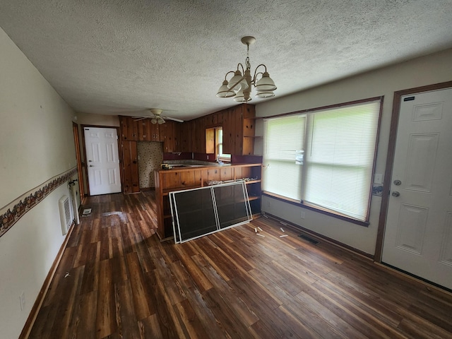 kitchen with a textured ceiling, brown cabinetry, baseboards, a peninsula, and dark wood-style flooring