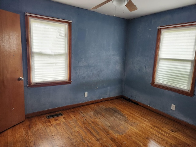 unfurnished room with plenty of natural light, a ceiling fan, visible vents, and wood-type flooring