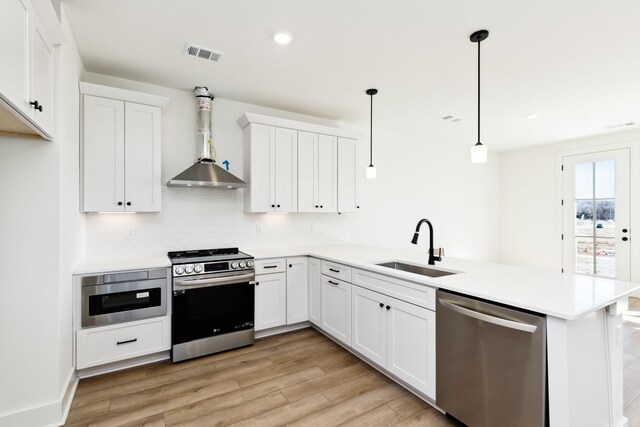 kitchen featuring a peninsula, light wood-style flooring, a sink, visible vents, and appliances with stainless steel finishes